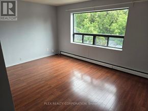 Toronto (Mimico) multi-family for rent - A room with wooden flooring and a large window showing greenery outside.