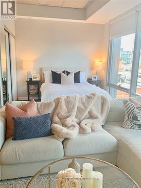 Toronto (Waterfront Communities) condo for rent - A bedroom with a white bed and a grey couch with a pink and blue pillow.