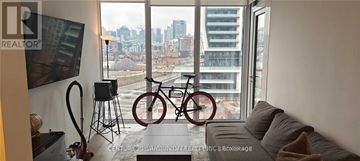 Toronto (Niagara) condo for rent - A living room with a couch and a bicycle in front of a window.