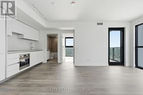 Toronto (Thorncliffe Park) condo for rent - A spacious, empty living room with a kitchen area to the left and a doorway leading to another room.