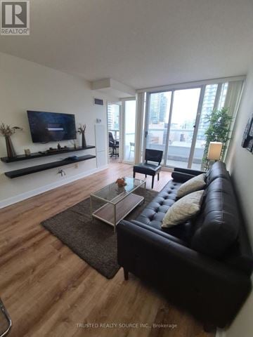 Toronto (Yonge-Eglinton) condo for rent - A living room with a black couch and a flat screen TV mounted on the wall.