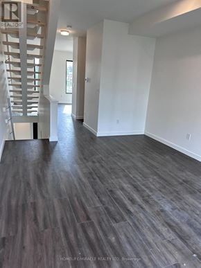 Barrie (Holly) townhouse for rent - A spacious room with wooden flooring and a staircase on the left side.