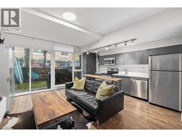 Vancouver apartment for rent - A modern kitchen and living room with a black couch and wooden coffee table.