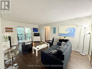 Lambton Shores (Grand Bend) condo for rent - A living room with a black couch, a white coffee table, and a painting on the wall.
