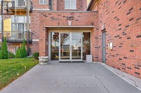 Hamilton (Waterdown) condo for rent - The entrance to a brick building with a glass door and a small garden in front.