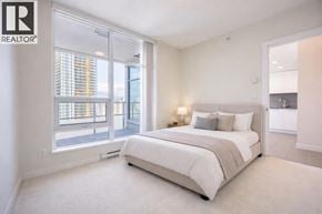 Burnaby apartment for rent - A bedroom with a large bed and a window overlooking a cityscape.
