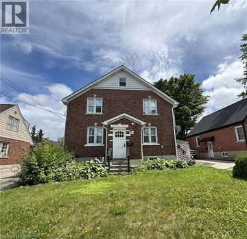 Kitchener apartment for rent - A brick house with a white door and windows is surrounded by greenery.