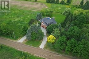 Caledon (Caledon Village) apartment for rent - A house with a red brick exterior and a black roof is surrounded by greenery.