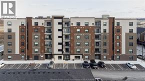 Tecumseh condo for rent - A large apartment building with a parking lot in front.
