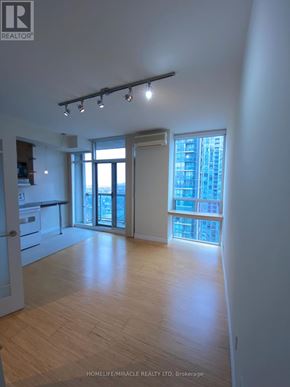 Mississauga (Fairview) condo for rent - A spacious room with wooden flooring and a large window overlooking a cityscape.