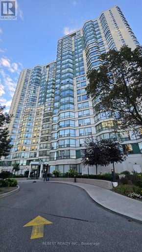 Mississauga (Hurontario) condo for rent - A tall building with many windows is shown with a yellow arrow on the road in front.