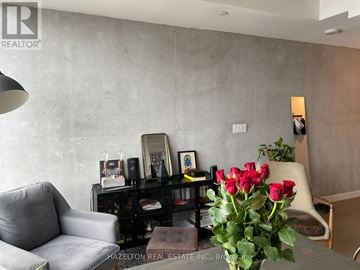 Toronto (Waterfront Communities) condo for rent - A living room with a grey couch, a coffee table, a vase of red roses, and a bookshelf with various items.