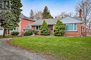 Toronto (Edenbridge-Humber Valley) apartment for rent - A house with a red brick exterior and a grey roof is surrounded by a green lawn and trees.