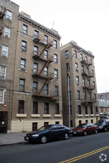 Bronx apartment for rent - A black car is parked in front of a tan building with a fire escape.