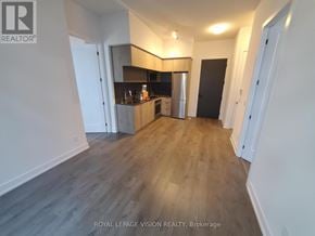 Toronto (Bayview Village) condo for rent - A spacious room with wooden flooring and white walls, featuring a kitchen area with a refrigerator, cabinets, and a countertop.