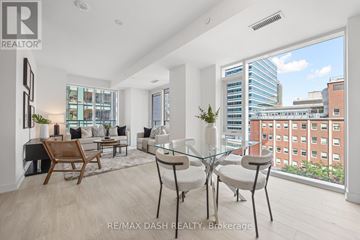 Toronto (Church-Yonge Corridor) condo for rent - A well-lit, modern living room with a glass table and chairs, a wooden chair, and a view of a cityscape through the window.