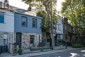 Toronto (South Riverdale) townhouse for rent - A house with a grey siding and a black door is surrounded by other houses and trees.
