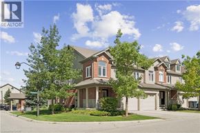 Guelph townhouse for rent - A house with a brown roof and a white garage door is surrounded by trees and other houses.