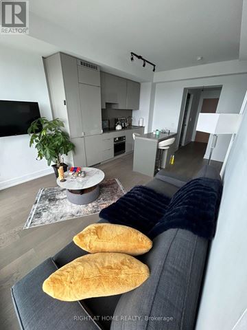 Toronto (Bay Street Corridor) condo for rent - A modern living room with a grey sofa and a grey kitchen in the background.