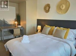 Barrie (Lakeshore) apartment for rent - A bedroom with a large bed, a nightstand with a plant, and two hats on the wall.