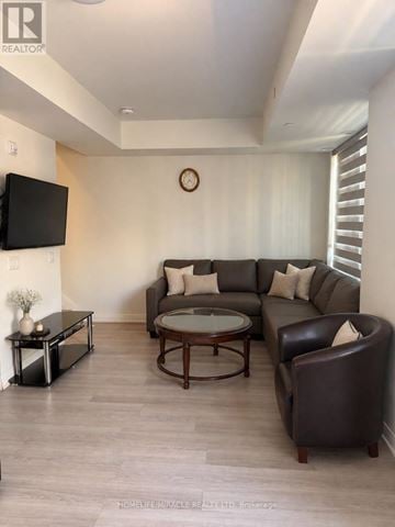 Brampton (Bram East) townhouse for rent - A living room with a brown leather couch, a glass coffee table, and a flat screen TV mounted on the wall.
