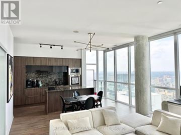 Toronto (Waterfront Communities) condo for rent - A modern kitchen with a dining table and chairs in the foreground and a view of the city in the background.