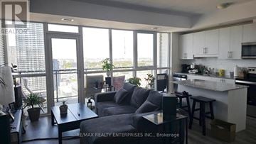 Kitchener condo for rent - A living room with a grey couch and a kitchen area with white cabinets.