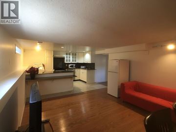 Vancouver apartment for rent - A living room with a red couch and a kitchen area in the background.