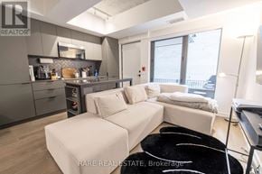 Toronto (Moss Park) townhouse for rent - A modern living room with a large couch and a kitchen area in the background.