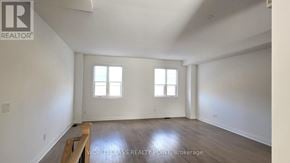 Whitby (Port Whitby) townhouse for rent - A spacious room with wooden flooring and two windows.