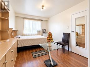 Toronto (Oakridge) triplex for rent - A bedroom with a bed, a chair, and a table with a vase of flowers on it.