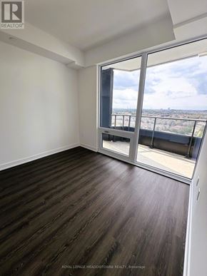 Mississauga (City Centre) condo for rent - A room with wooden flooring and a large window overlooking a cityscape.
