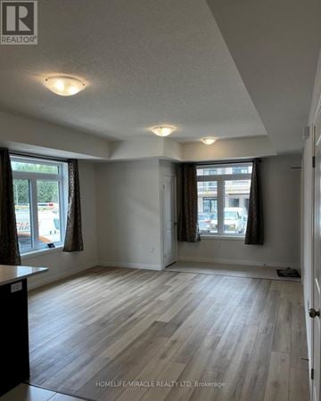 Guelph (Kortright East) townhouse for rent - A room with wooden flooring and two windows with curtains.