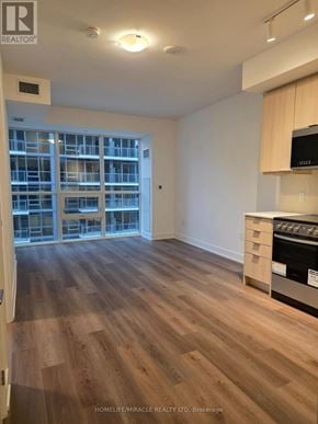 Milton (Tm Timberlea) condo for rent - A spacious room with wooden flooring and a kitchen area with a stove.