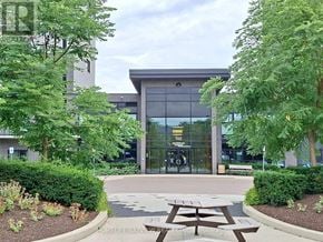 Oakville (Go Glenorchy) condo for rent - A building with a glass facade and a sign that reads "102" is surrounded by greenery and has a picnic table in front.