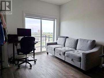 Oakville (Go Glenorchy) condo for rent - A living room with a grey couch and a black office chair.