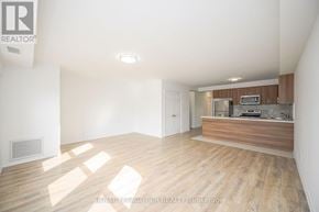 Orangeville multi-family for rent - A well-lit, empty room with wooden flooring and a kitchenette in the background.