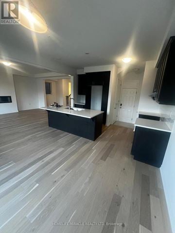 Barrie (Painswick South) apartment for rent - A spacious room with wooden flooring and a kitchen area with black cabinets and a countertop.