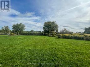 East Gwillimbury apartment for rent - A large, open grassy field with a few trees and bushes in the distance under a partly cloudy sky.