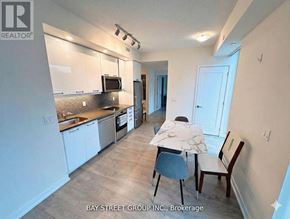 Toronto (Waterfront Communities) condo for rent - A kitchen with white cabinets and a counter with a chair and a person sitting at it.