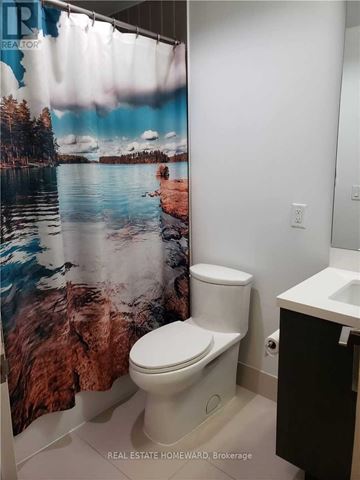 Toronto (Waterfront Communities) condo for rent - A white toilet in a bathroom with a shower curtain featuring a lake and forest scene.