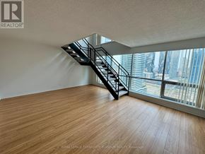 Toronto (Waterfront Communities) condo for rent - A room with wooden flooring and a staircase leading to a balcony with a view of the city.