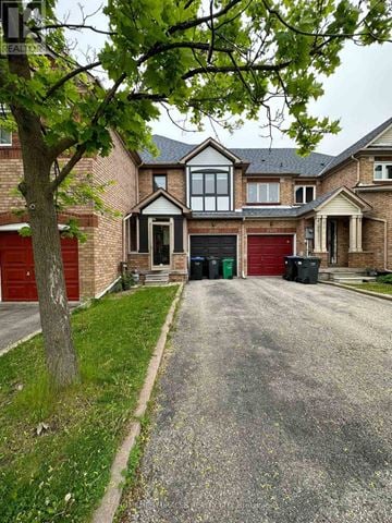 Mississauga (Lisgar) townhouse for rent - A house with a red garage door is surrounded by a gravel driveway and a tree.