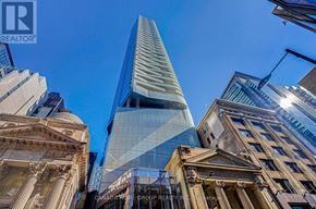 Toronto (Church-Yonge Corridor) condo for rent - A tall, modern glass skyscraper stands in the center of a cityscape, surrounded by older buildings with classical architecture.