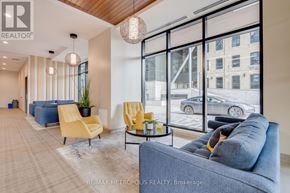Kitchener condo for rent - A living room with a grey couch, yellow chairs, and a large window overlooking a parking lot.