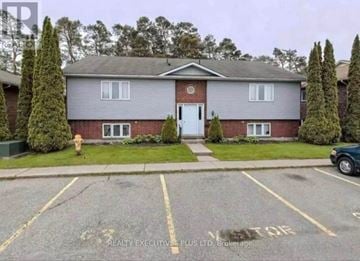 Orangeville multi-family for rent - A house with a grey roof and a white door is surrounded by a parking lot.