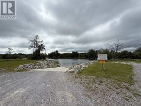 Otonabee-South Monaghan apartment for rent - A sign stands in a grassy area by a body of water under a cloudy sky.