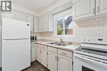 Sarnia apartment for rent - A white refrigerator stands in a kitchen with white cabinets and a white stove.