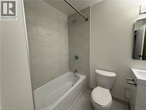 Brantford condo for rent - A white toilet is in a bathroom with a white tub and sink.