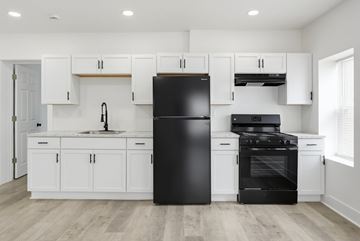 Ashtabula apartment for rent - A black refrigerator stands in a kitchen with white cabinets and a black stove.